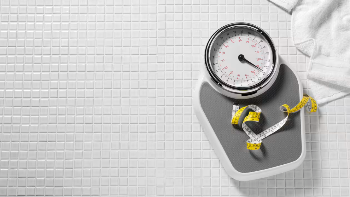Bathroom scale with measuring tape on tiled floor symbolising weight management