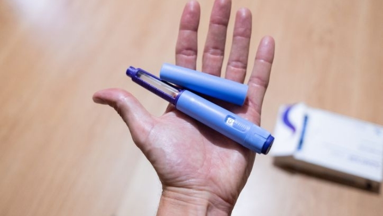 Hand holding blue injectable pen device with cap removed